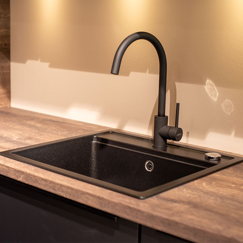 Close-up van een zwarte kraan met ronde uitloop en spoelbak in houten keukenblad