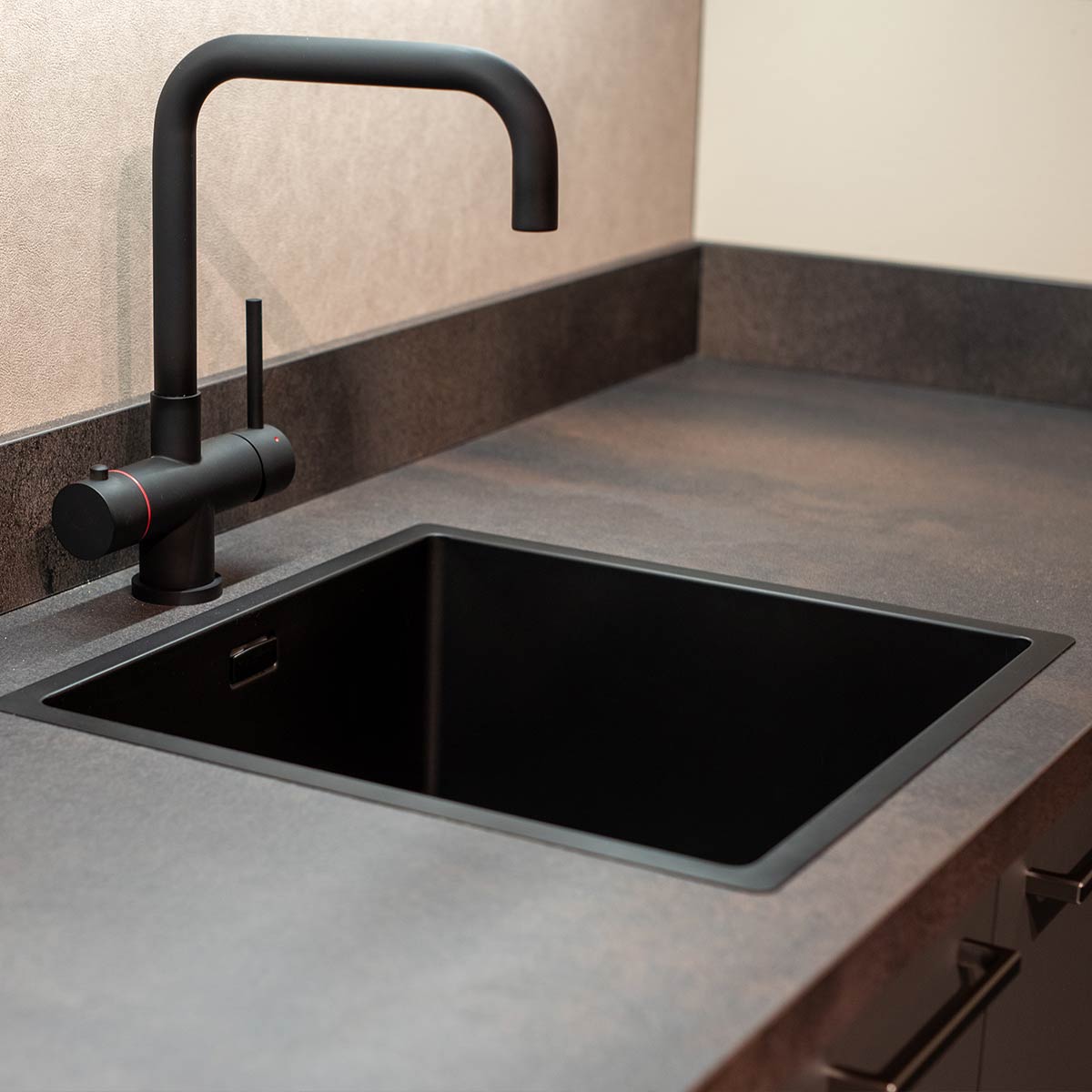 Close-up van een moderne zwarte kraan met rechte uitloop en vierkante spoelbak in donker werkblad