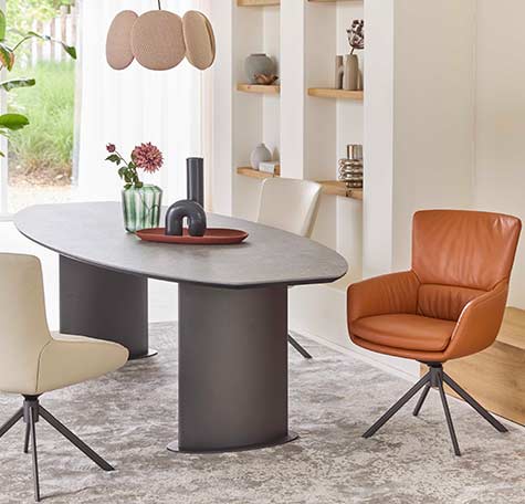 Ovale eettafel met donker blad en moderne kuipstoelen in leer en stof van Bert Plantagie, in lichte eetkamer met designlamp en open wandplanken