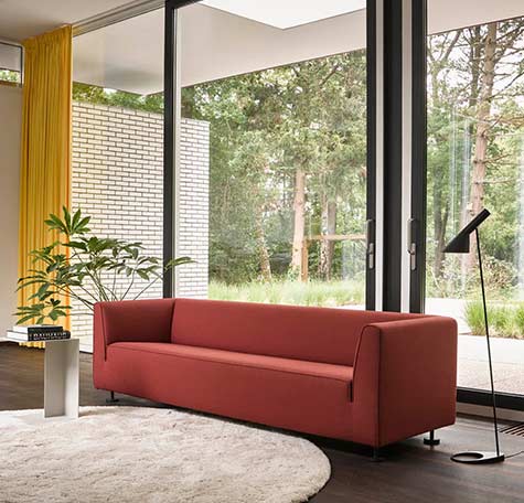 Rode designbank van Gelderland Design met strakke belijning in moderne woonkamer met grote ramen, geel gordijn en zwart leeslampje