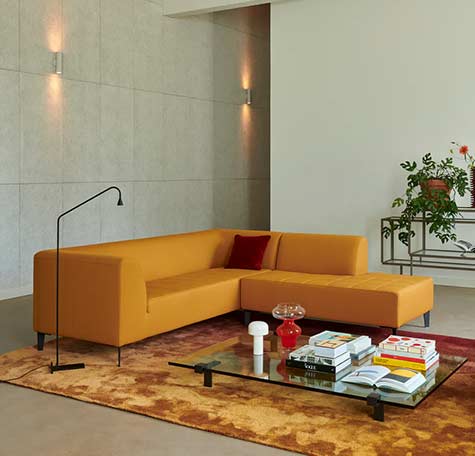 Gele hoekbank met chaise longue van Gelderland Design op roodbruin vloerkleed in moderne woonkamer met glazen salontafel en strakke wandlampen
